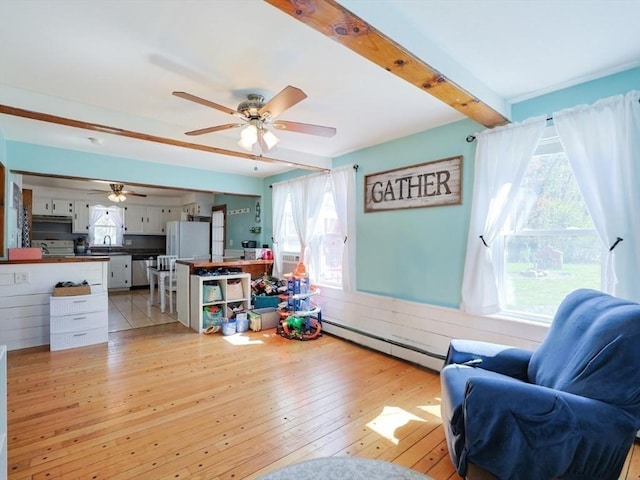 living area featuring ceiling fan, a wealth of natural light, baseboard heating, and light wood-style flooring