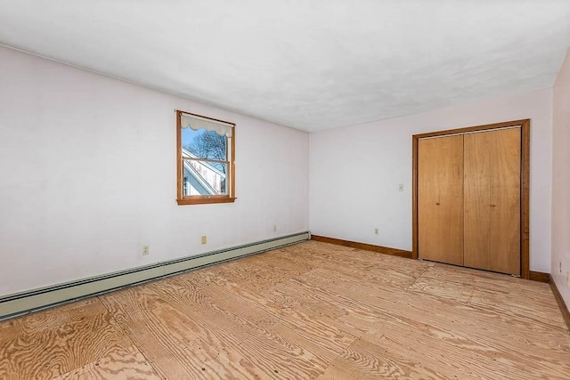 unfurnished bedroom featuring a baseboard heating unit, a closet, and light wood-type flooring