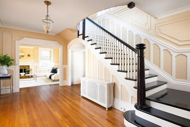 87 Crowninshield Rd, Brookline, MA 02446 - stairway featuring an inviting chandelier, ornamental molding, wood finished floors, and a decorative wall