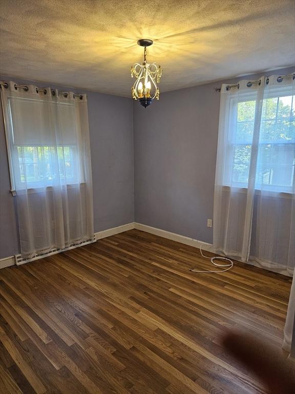 spare room featuring a chandelier, dark wood finished floors, baseboards, and a textured ceiling