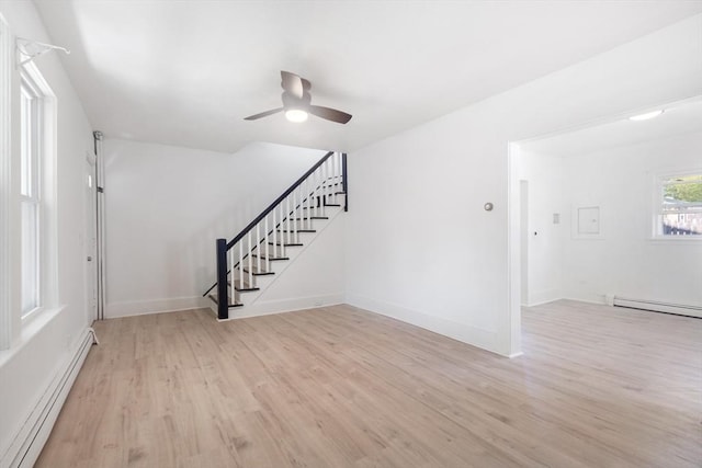 unfurnished living room featuring light wood-style floors, a ceiling fan, stairs, and a baseboard heating unit