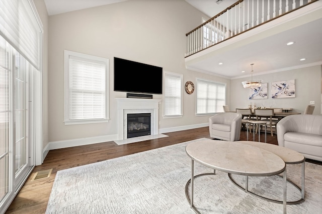 living room featuring a towering ceiling, crown molding, hardwood / wood-style flooring, and a chandelier