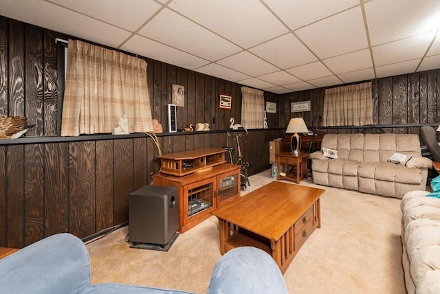 living room with a drop ceiling, light colored carpet, and wood walls