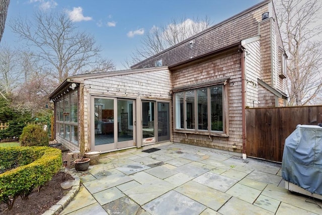 back of property with fence, a sunroom, a patio, and roof with shingles