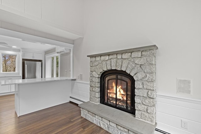 details with freestanding refrigerator, a wall unit AC, wood finished floors, a stone fireplace, and a baseboard heating unit