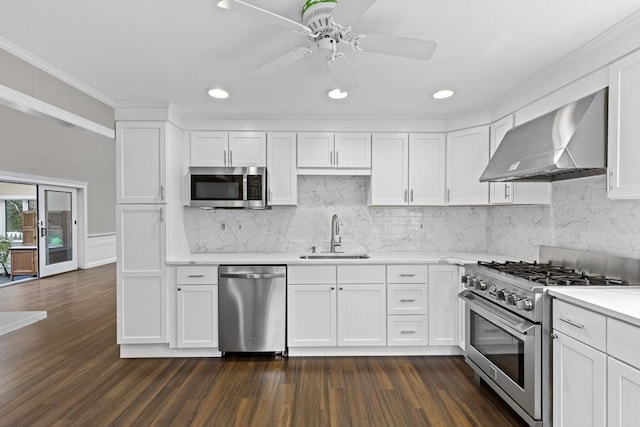 kitchen with white cabinets, a ceiling fan, appliances with stainless steel finishes, a sink, and wall chimney range hood