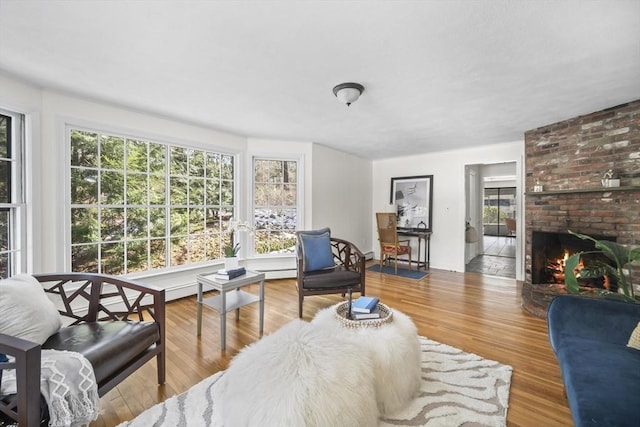 living area with a brick fireplace, wood finished floors, and a baseboard radiator