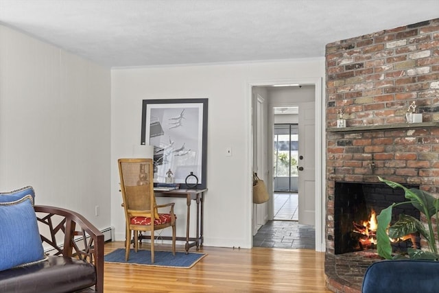 sitting room featuring a brick fireplace, baseboards, and wood finished floors