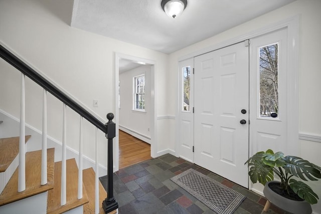 entrance foyer featuring a baseboard radiator, stone finish flooring, baseboards, and stairs