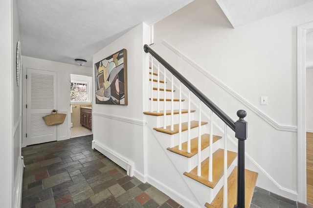 stairway featuring a baseboard heating unit and stone tile floors