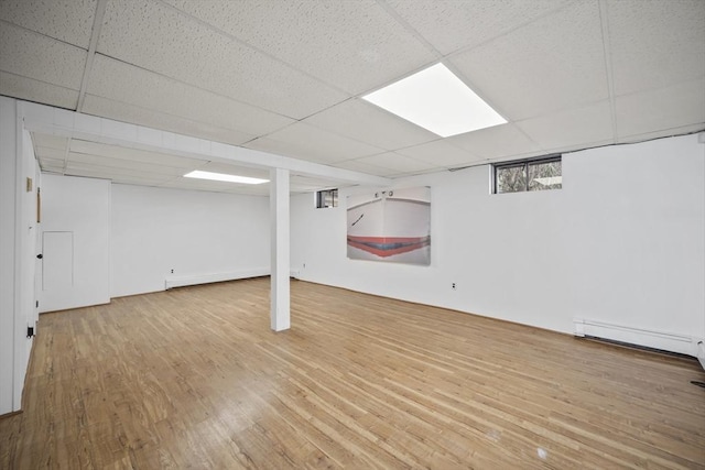 below grade area featuring baseboard heating, a drop ceiling, and wood finished floors