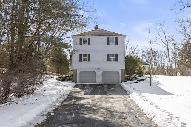 view of snow covered exterior with aphalt driveway, a chimney, and an attached garage