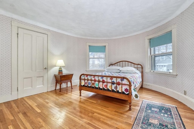 bedroom featuring baseboards, light wood finished floors, and wallpapered walls