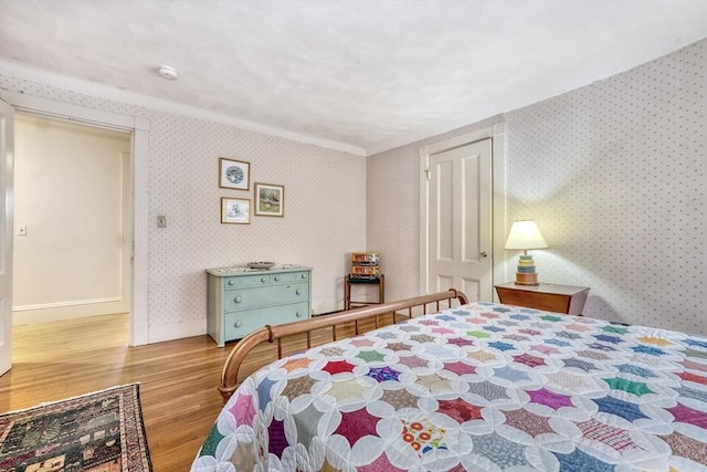 bedroom featuring baseboards, wood finished floors, and wallpapered walls