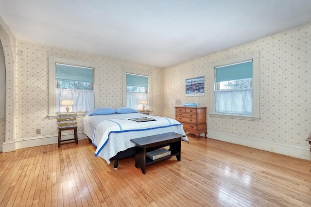 bedroom featuring wallpapered walls, wood-type flooring, multiple windows, and baseboards