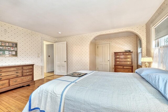 bedroom with arched walkways, wood finished floors, and wallpapered walls