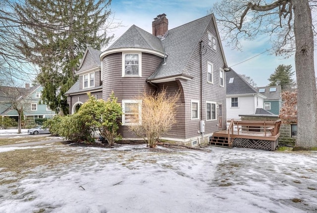 view of snow covered exterior featuring roof with shingles, a chimney, and a wooden deck