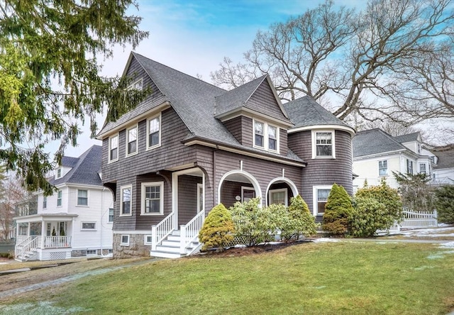 shingle-style home featuring a porch, roof with shingles, and a front lawn