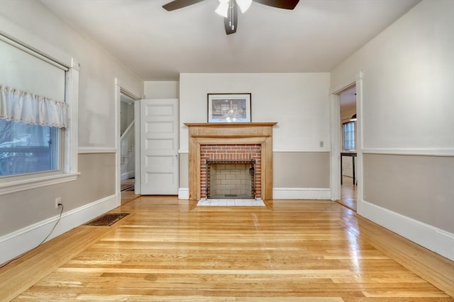 unfurnished living room with baseboards, visible vents, a ceiling fan, wood finished floors, and a brick fireplace