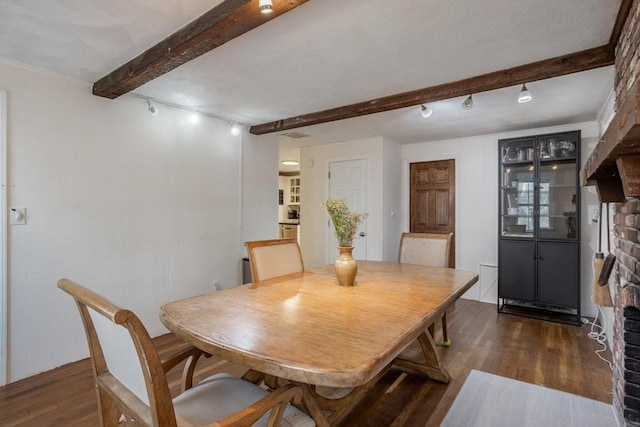 dining area with rail lighting, a fireplace, dark wood-type flooring, and beam ceiling