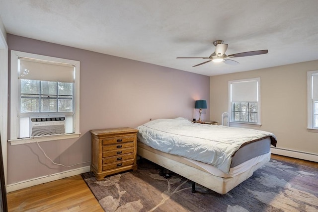 bedroom featuring a baseboard radiator, cooling unit, wood finished floors, a ceiling fan, and baseboards