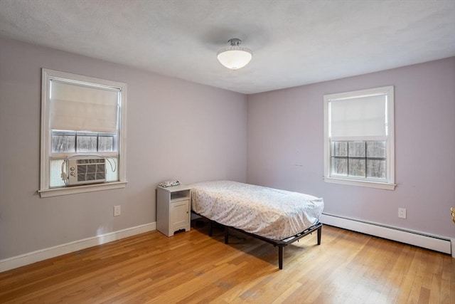 bedroom with light wood finished floors, a baseboard radiator, baseboards, and cooling unit