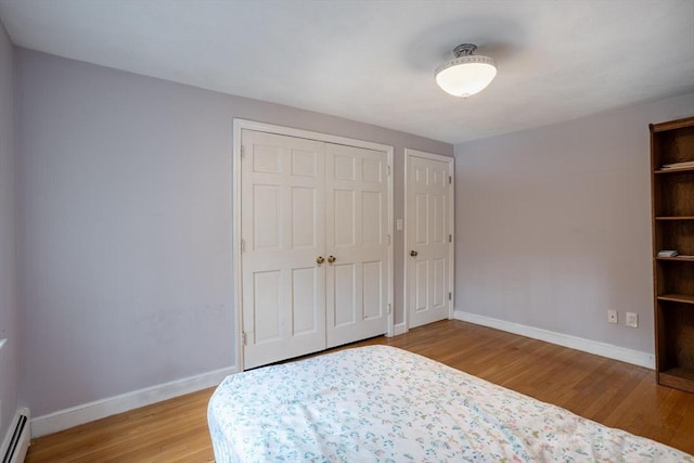 unfurnished bedroom featuring a baseboard heating unit, a closet, baseboards, and light wood-style floors