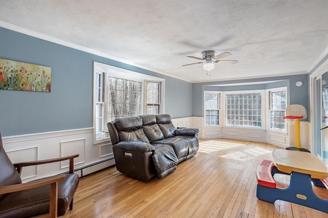 living area with a textured ceiling, ornamental molding, wainscoting, and light wood-style flooring