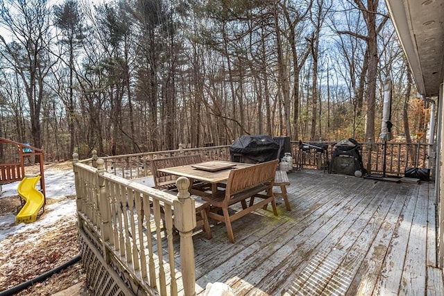 wooden deck featuring a grill, a playground, and outdoor dining space