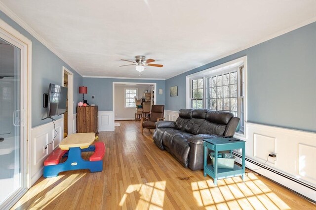 living area with a baseboard heating unit, ceiling fan, a wainscoted wall, and wood finished floors