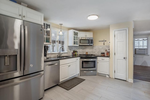 kitchen with stainless steel appliances, a sink, white cabinets, dark countertops, and glass insert cabinets