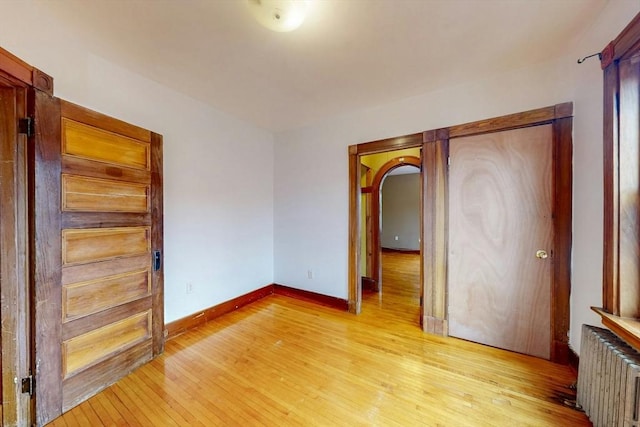 76 Belden St, Boston, MA 02125 - empty room with radiator, light wood finished floors, baseboards, and arched walkways