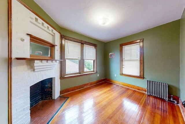 76 Belden St, Boston, MA 02125 - unfurnished living room featuring radiator heating unit, wood-type flooring, a brick fireplace, and baseboards