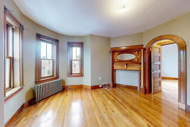 76 Belden St, Boston, MA 02125 - unfurnished room featuring radiator heating unit, light wood finished floors, arched walkways, and baseboards