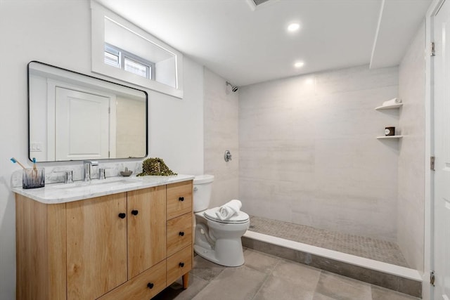 bathroom featuring a tile shower, vanity, and toilet