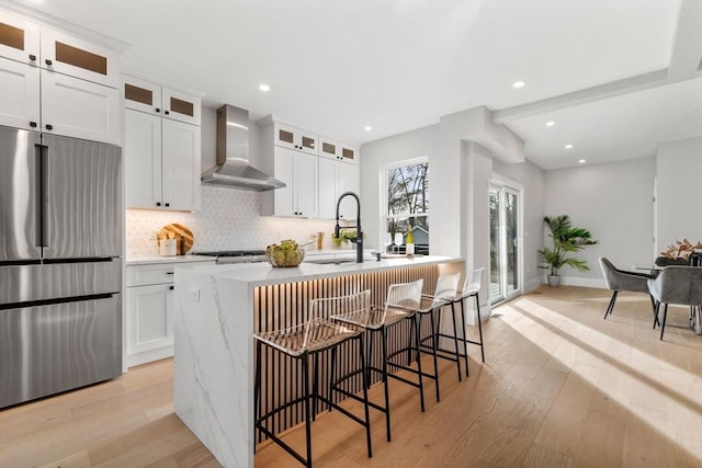 kitchen featuring white cabinets, stainless steel fridge, wall chimney exhaust hood, and sink