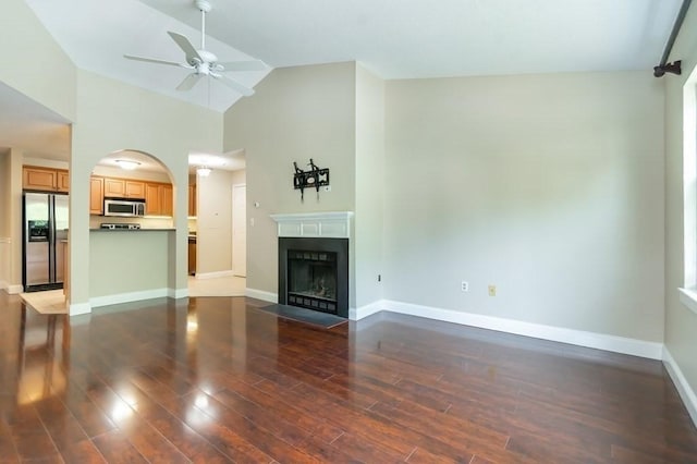 unfurnished living room featuring ceiling fan, wood finished floors, a fireplace with flush hearth, baseboards, and high vaulted ceiling