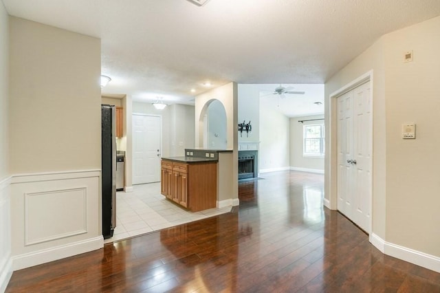 kitchen featuring dark countertops, a ceiling fan, a fireplace with flush hearth, freestanding refrigerator, and light wood-style floors