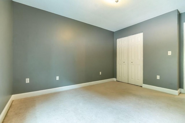 unfurnished bedroom featuring light colored carpet, a closet, and baseboards