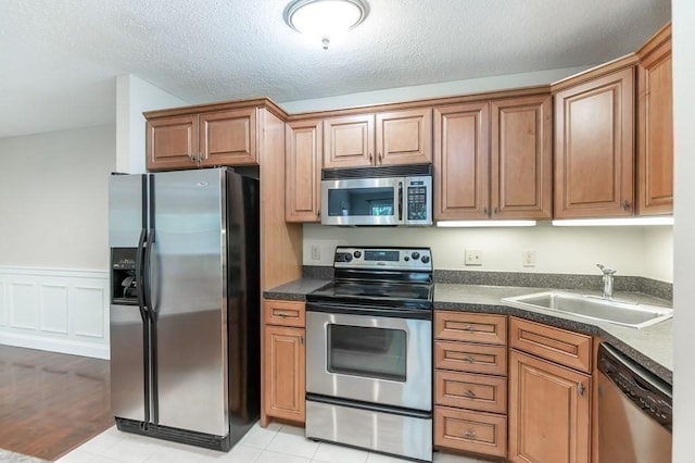 kitchen with stainless steel appliances, a sink, dark countertops, brown cabinetry, and a textured ceiling
