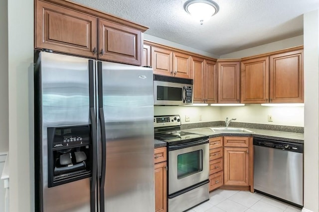 kitchen featuring appliances with stainless steel finishes, a sink, dark countertops, light tile patterned floors, and a textured ceiling