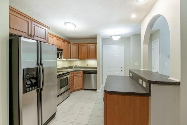 kitchen with appliances with stainless steel finishes, dark countertops, a sink, light tile patterned floors, and a textured ceiling