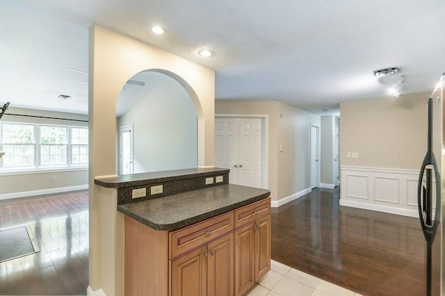 kitchen with dark countertops, freestanding refrigerator, light wood-style floors, brown cabinets, and recessed lighting