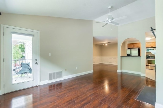 unfurnished living room with wood finished floors, a ceiling fan, lofted ceiling, a wainscoted wall, and arched walkways