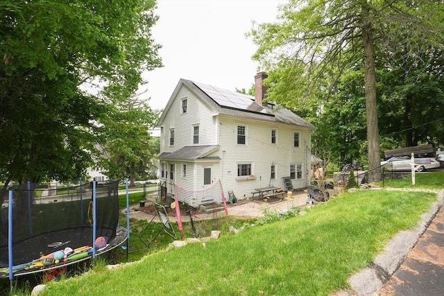 1013 Pleasant St, Worcester, MA 01602 - rear view of property with a trampoline, a chimney, a yard, and solar panels