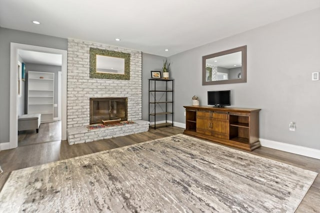 unfurnished living room featuring a brick fireplace, recessed lighting, wood finished floors, and baseboards