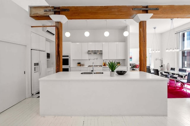 kitchen featuring a center island with sink, white cabinetry, decorative light fixtures, and white fridge with ice dispenser