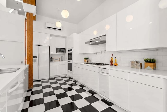 kitchen featuring built in appliances, a wall mounted AC, tasteful backsplash, sink, and white cabinets