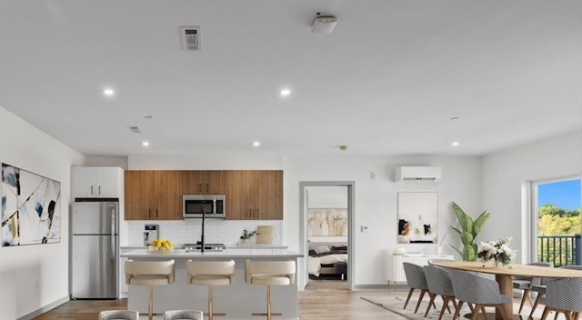 kitchen featuring a wall mounted air conditioner, decorative backsplash, stainless steel appliances, light hardwood / wood-style floors, and white cabinetry