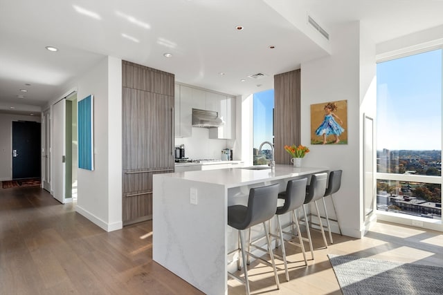 kitchen featuring kitchen peninsula, gas cooktop, a breakfast bar area, light hardwood / wood-style floors, and ventilation hood